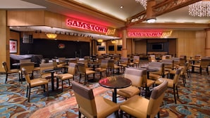 A hotel lobby with multiple seating areas, a stage, and a neon sign reading "SAM'S TOWN".