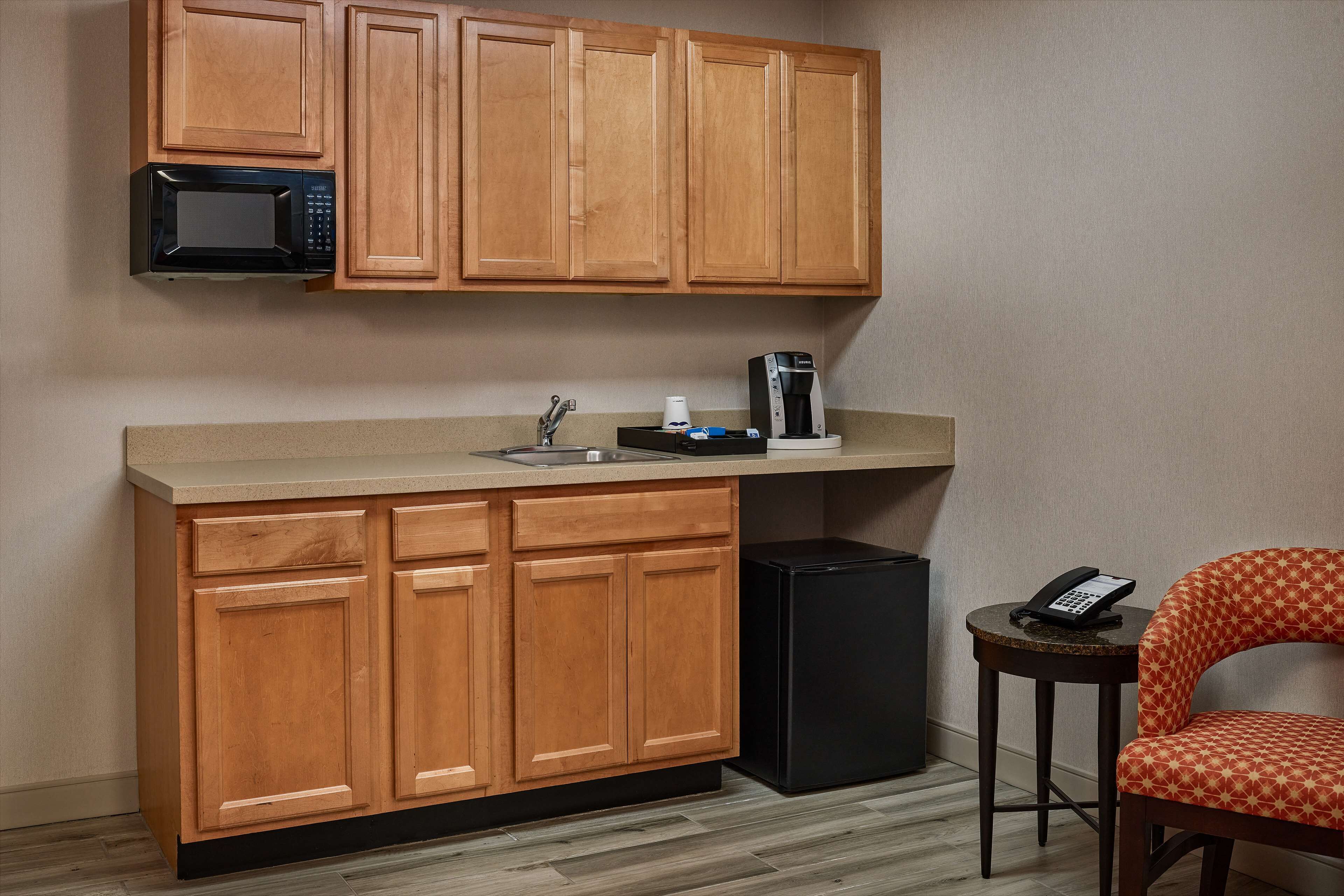 A compact kitchen with wooden cabinets, a microwave, a coffee maker, and a refrigerator.