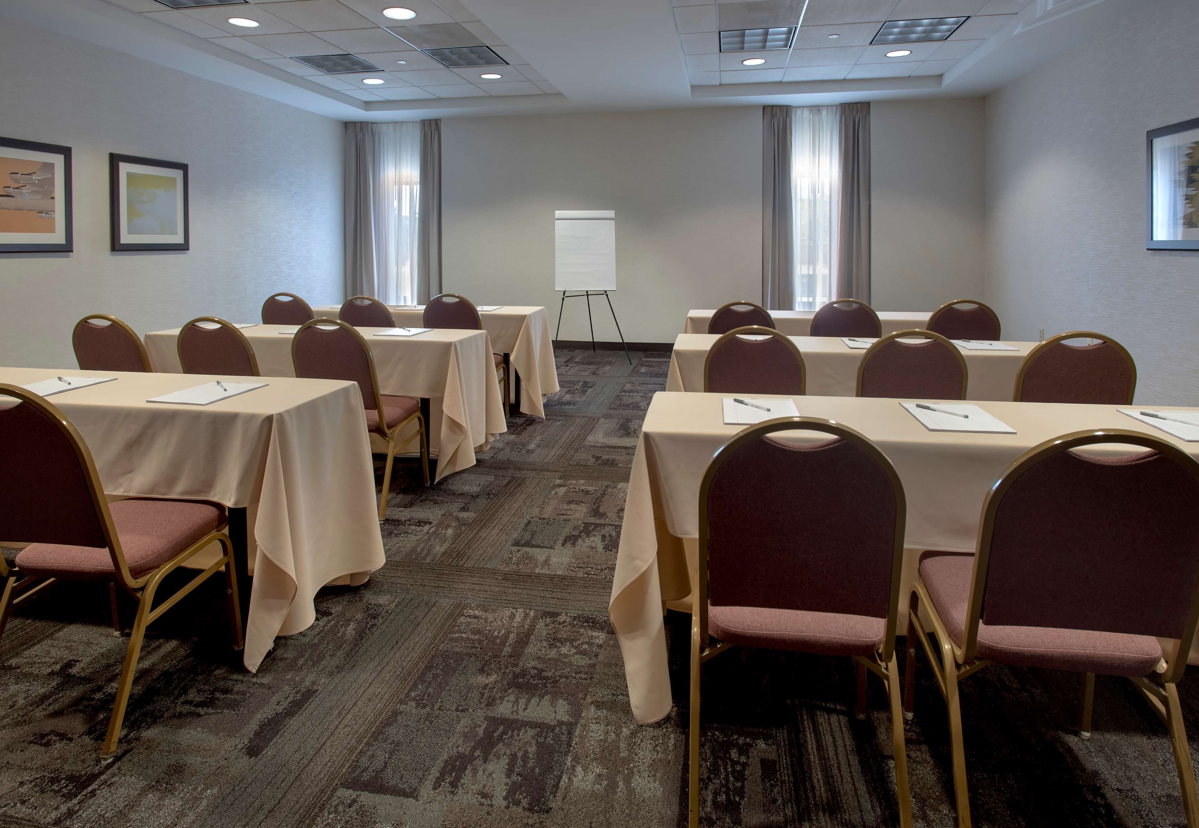 Sala de conferências com mesas, cadeiras, quadro branco e piso coberto de carpete.