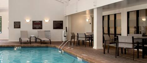 An indoor swimming pool with clear water, surrounded by lounge chairs and a dining area.