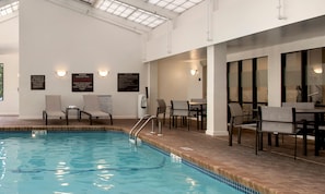 Una piscina interior con agua cristalina, rodeada de sillones de descanso y un comedor.