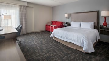 A hotel room with a large bed, a desk with a chair, a red sofa, and two bedside lamps.