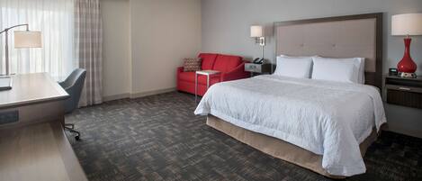 Habitación de hotel con una cama grande, un escritorio con silla, un sofá rojo y dos lámparas de noche.