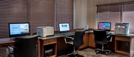 Una oficina moderna con dos escritorios, cada uno con una computadora e impresora, y dos sillas de oficina negras.