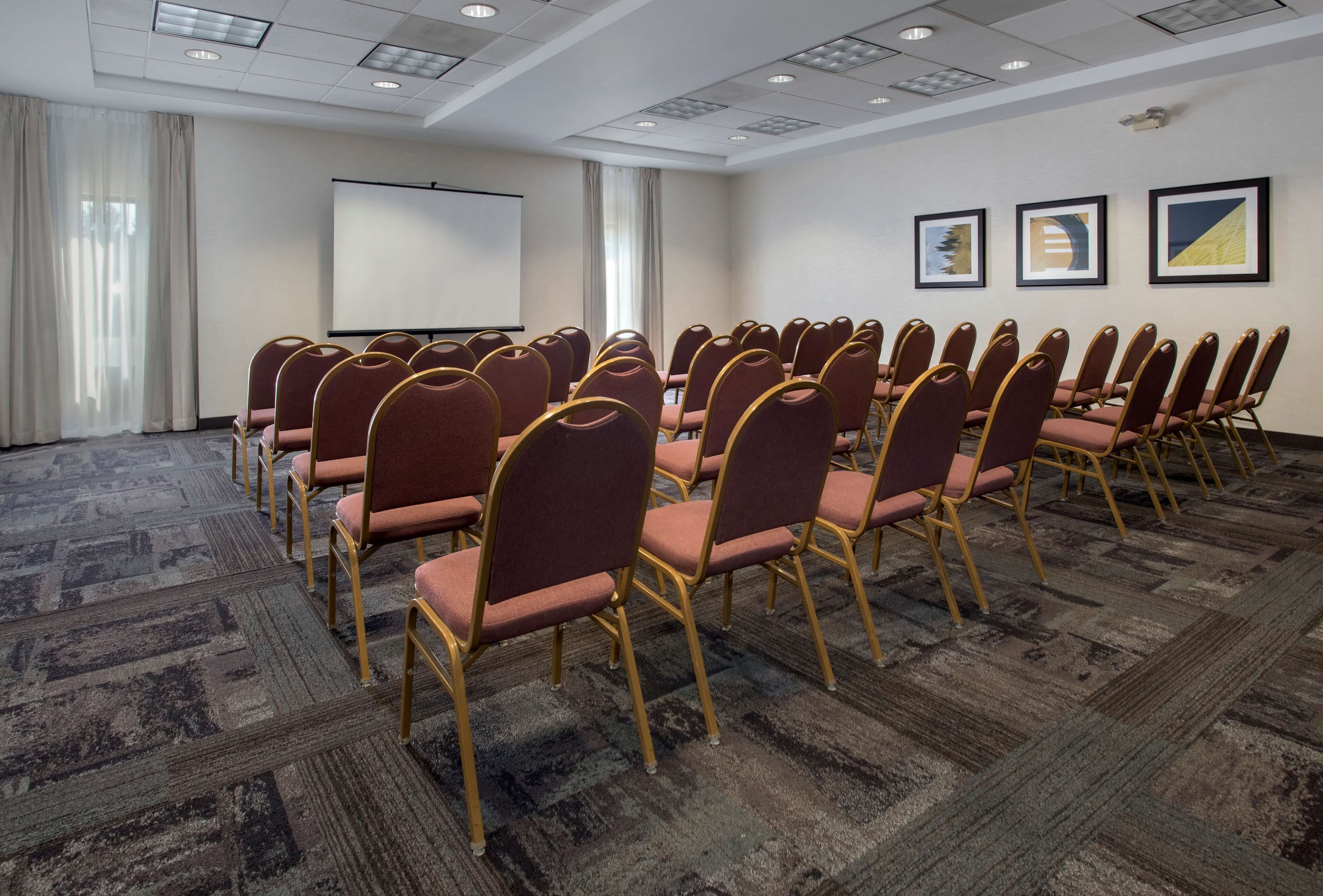 A conference room with rows of chairs, a projector screen, and framed artwork on the wall.