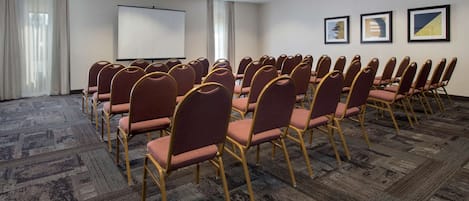 A conference room with rows of chairs, a projector screen, and framed artwork on the wall.