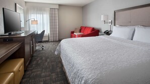 Ein Hotelzimmer mit einem großen Bett, einem Schreibtisch mit Fernseher, einem roten Sessel, einem kleinen Tisch und einem Telefon auf dem Nachttisch.