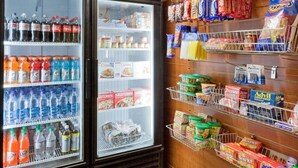 Ein gekühlter Warenpräsentierer mit Getränken und Snacks, und eine Wand mit aufgehängten Einkaufstaschen.