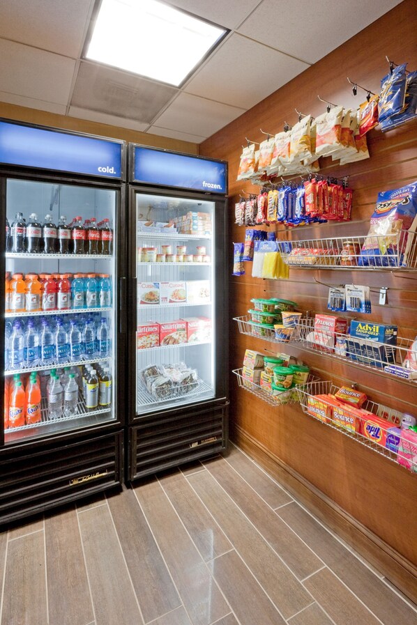 A refrigerated display with beverages and snacks, and a wall with hanging bags of groceries.