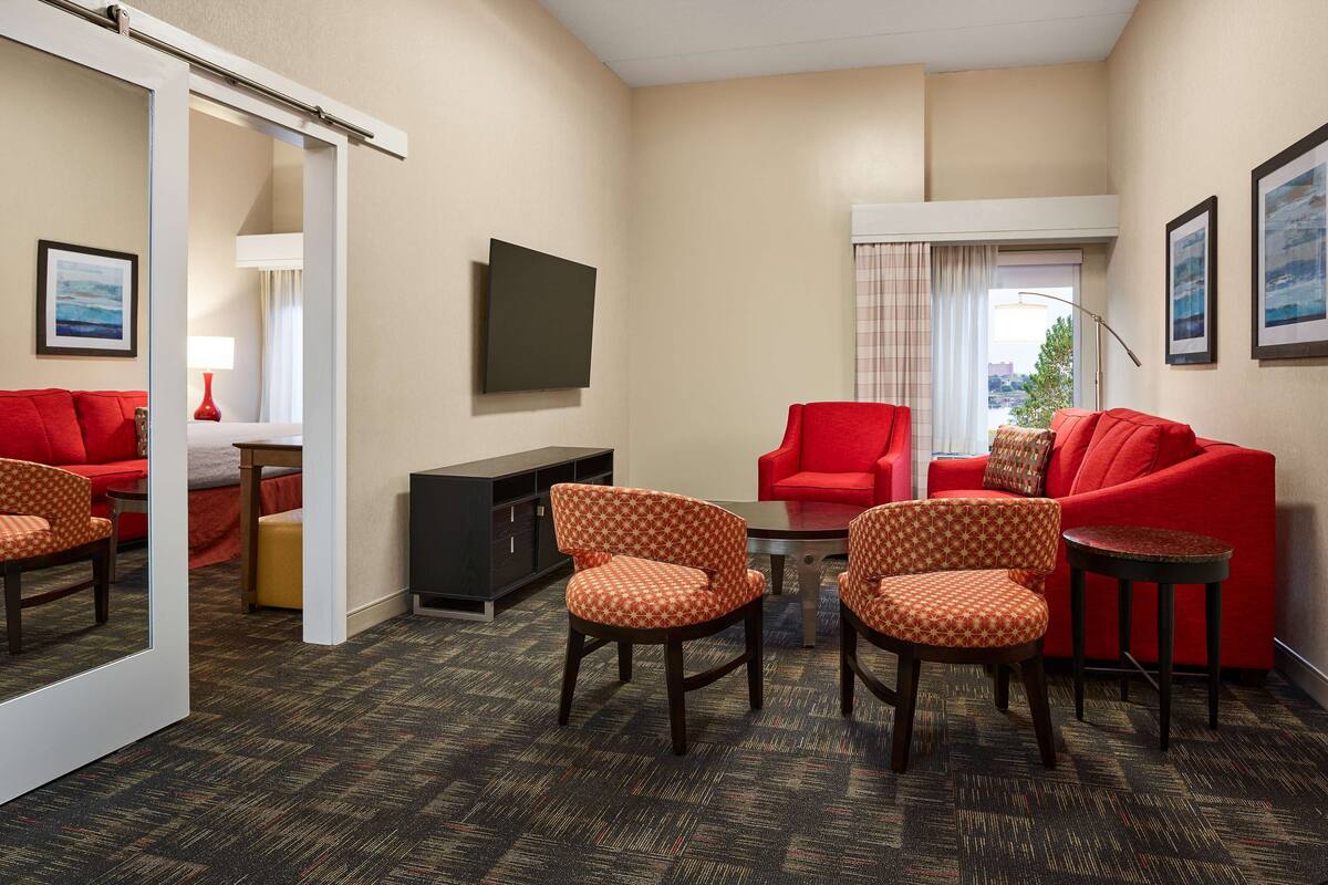 A hotel room with a red sofa, matching armchairs, a small table, and a TV mounted on the wall.