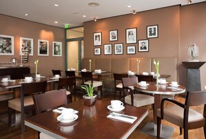 Un comedor de hotel con varias mesas y sillas, cuadros en la pared y una planta en una mesa.