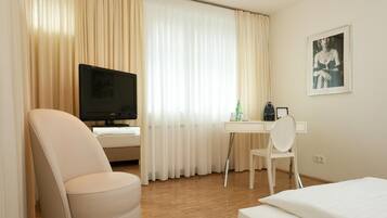 Ein Hotelzimmer mit einem Bett, einem Schreibtisch mit Stuhl, einem Fernseher und einem gerahmten Bild an der Wand.