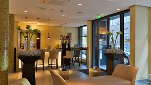 Un moderno vestíbulo de hotel con mostrador de recepción, zona de estar y amplias ventanas que dan a la calle.