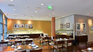 Un comedor de hotel con varias mesas y sillas, un mostrador de buffet y cuadros en las paredes.