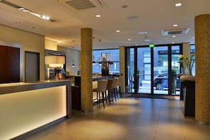 Un vestíbulo de hotel con recepción, zona de bar y asientos.