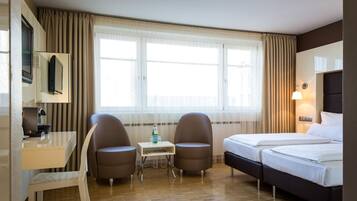 Una habitación de hotel con cama, escritorio, dos sillas, televisor y ventana con cortinas.