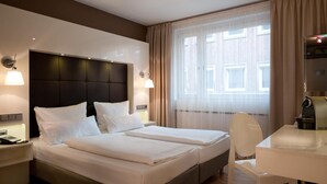Una habitación de hotel con cama doble, un escritorio y una silla, y un ventanal con cortinas.