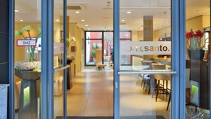 Una entrada de hotel con un mostrador de recepción, un cartel que dice "HOTEL SANTO" y una puerta de cristal con un letrero "BMZ".