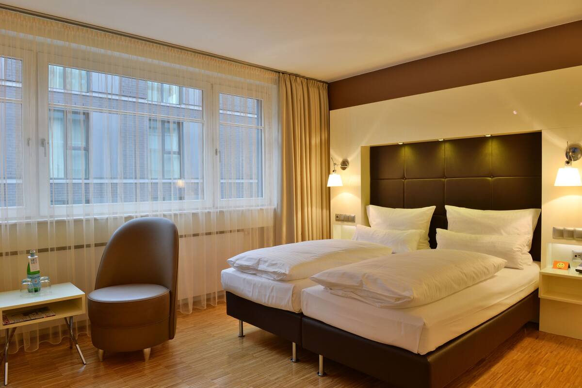 Une chambre d’hôtel avec un grand lit, une chaise, un bureau et une fenêtre avec des rideaux.
