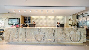 A hotel reception desk with marble detailing, a digital clock, and a security camera.