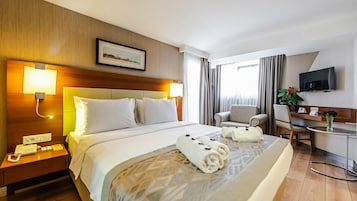 A hotel room with a large bed, bedside lamps, a desk with a chair, a TV, and a window with curtains.