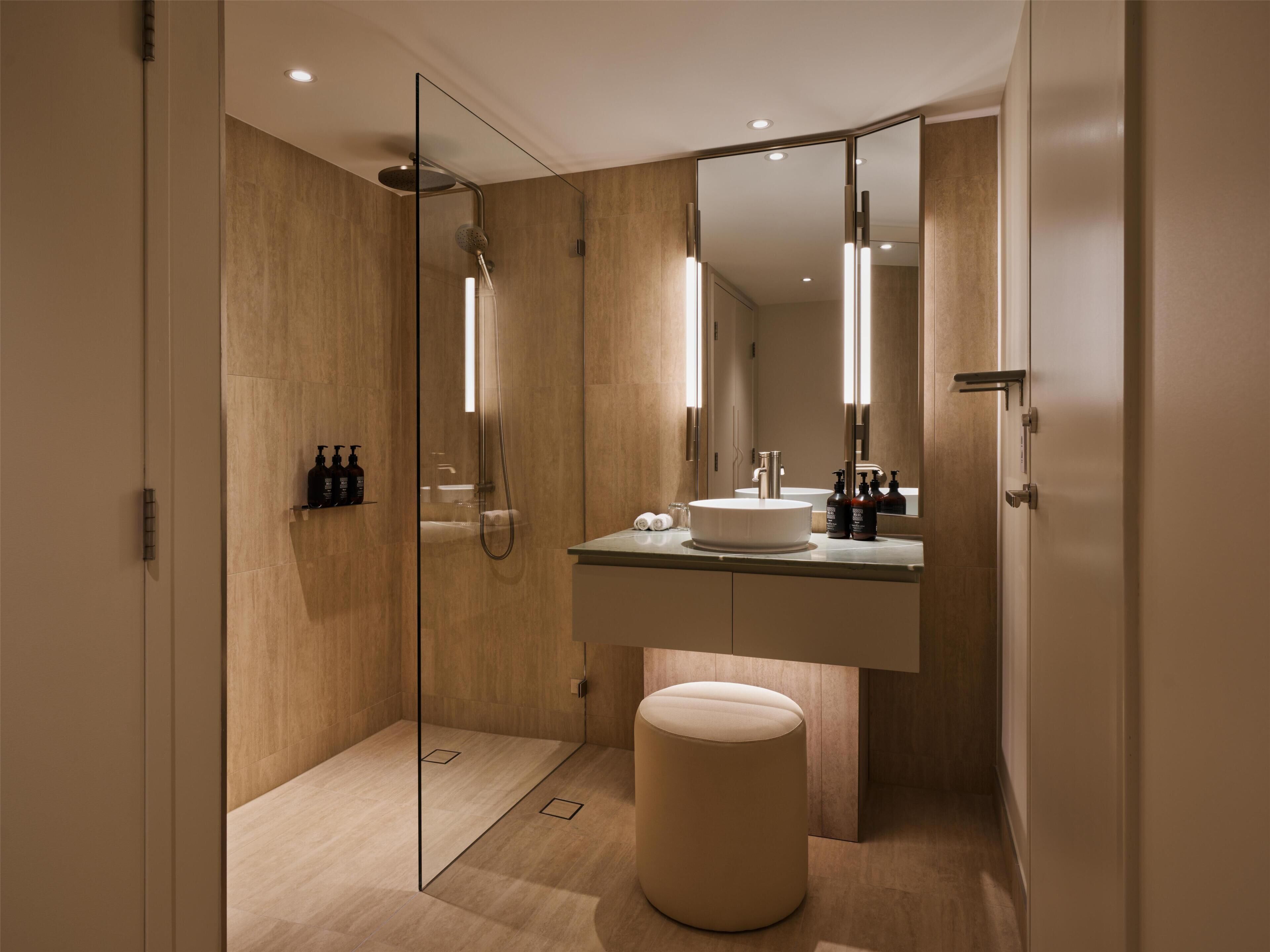 A modern bathroom with a glass-enclosed shower, a vanity with a mirror, and a round stool.