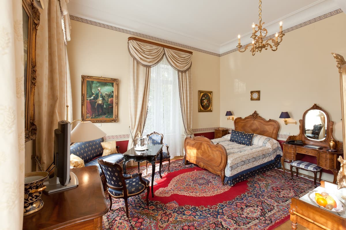 A traditional bedroom with a large bed, a desk, a chair, a television, and a chandelier.