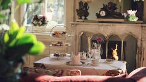 A dining table with a three-tiered dessert stand, a vase with flowers, and a fireplace in the background.