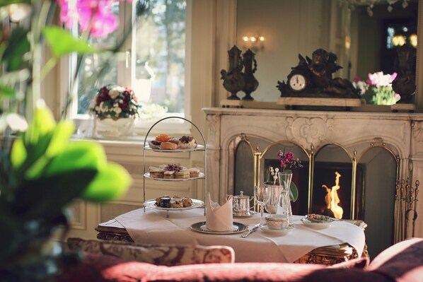 A dining table with a three-tiered dessert stand, a vase with flowers, and a fireplace in the background.