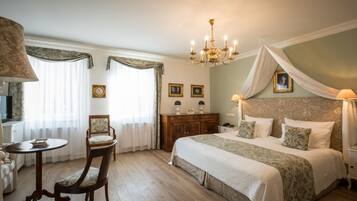 Quarto com uma cama grande, uma cadeira de madeira, uma mesinha e um candelabro.