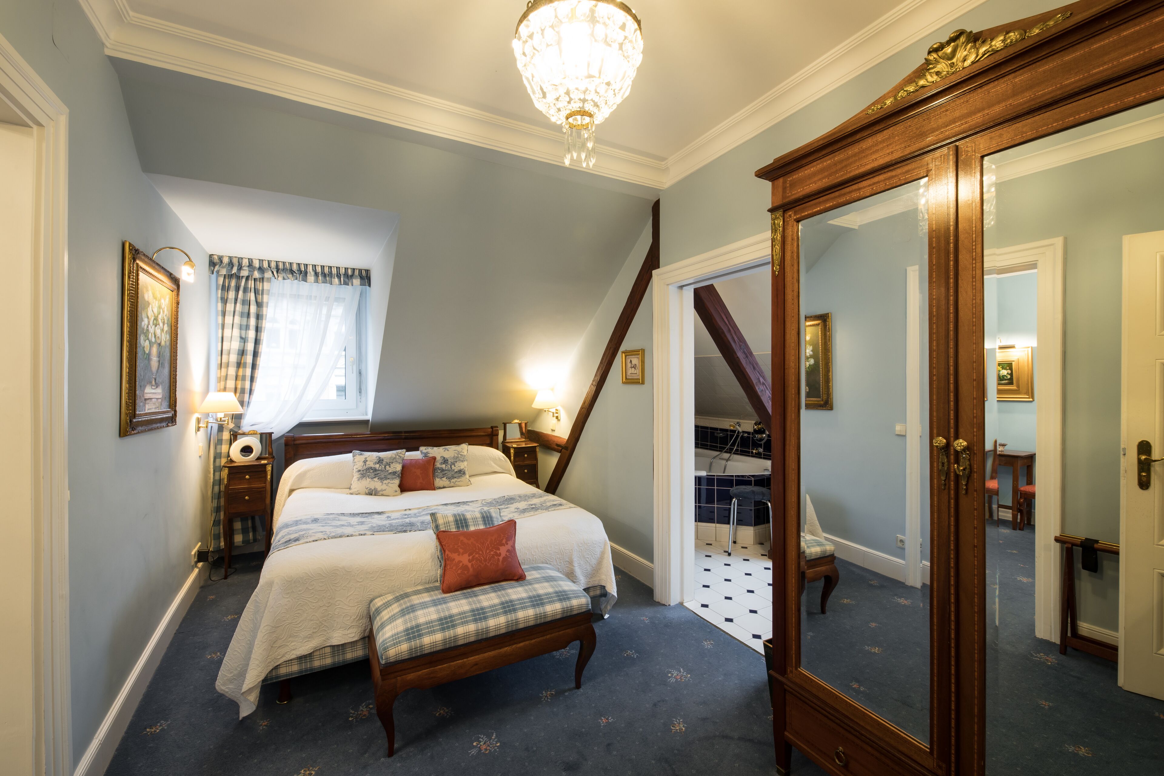 A bedroom with a large bed, a mirror, a chandelier, and a staircase leading to another room.