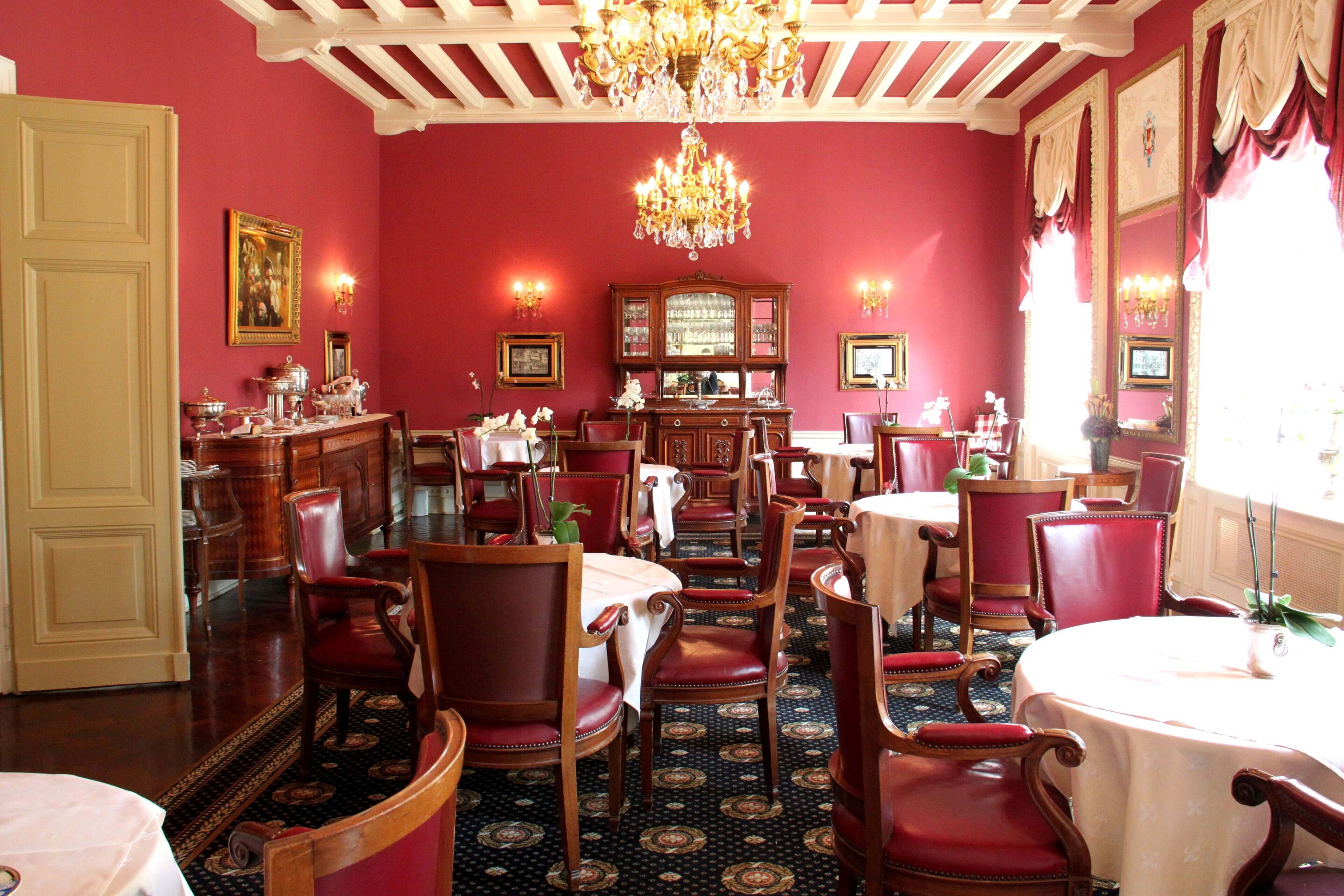 A dining area with red walls, wooden chairs, and a chandelier.