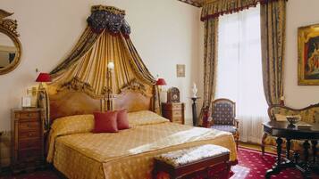 A large, ornate four-poster bed with a canopy, a wooden nightstand, a chair, and a table with a vase.