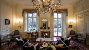 A formal room with a fireplace, chandeliers, and a dining table with chairs.