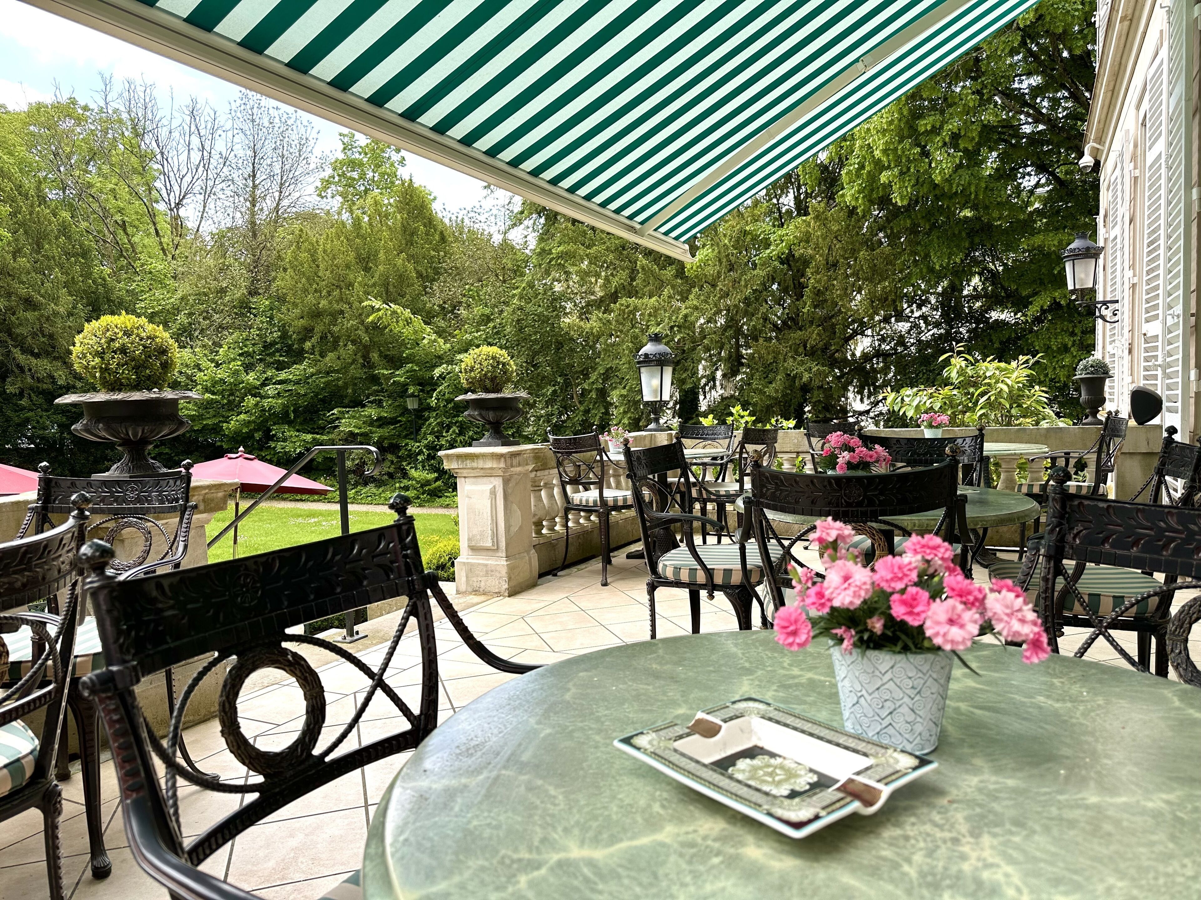 Une terrasse extérieure avec des tables rondes, des chaises noires et un auvent à rayures vertes.