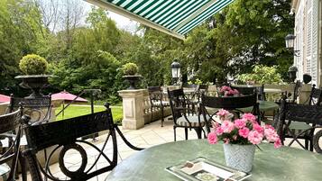 Une terrasse extérieure avec des tables rondes, des chaises noires et un auvent à rayures vertes.