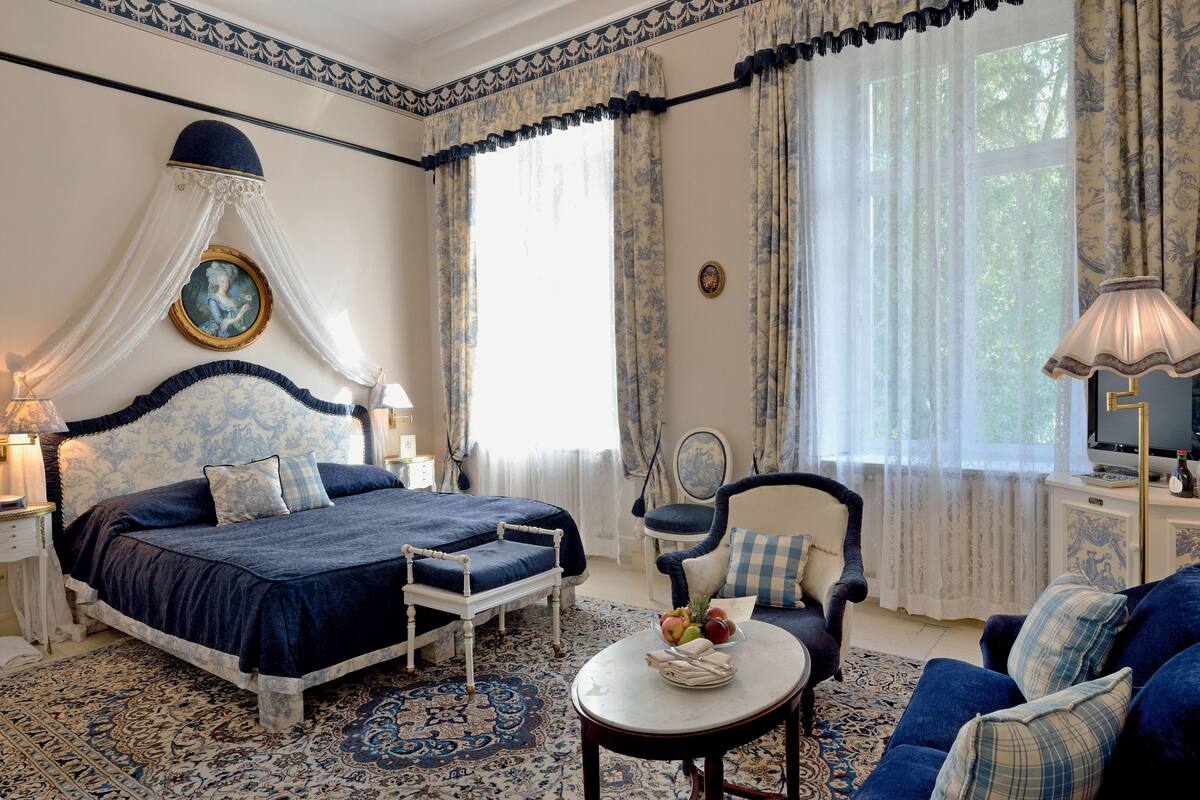 A bedroom with a large bed, a chair, a table with fruit, and a television.