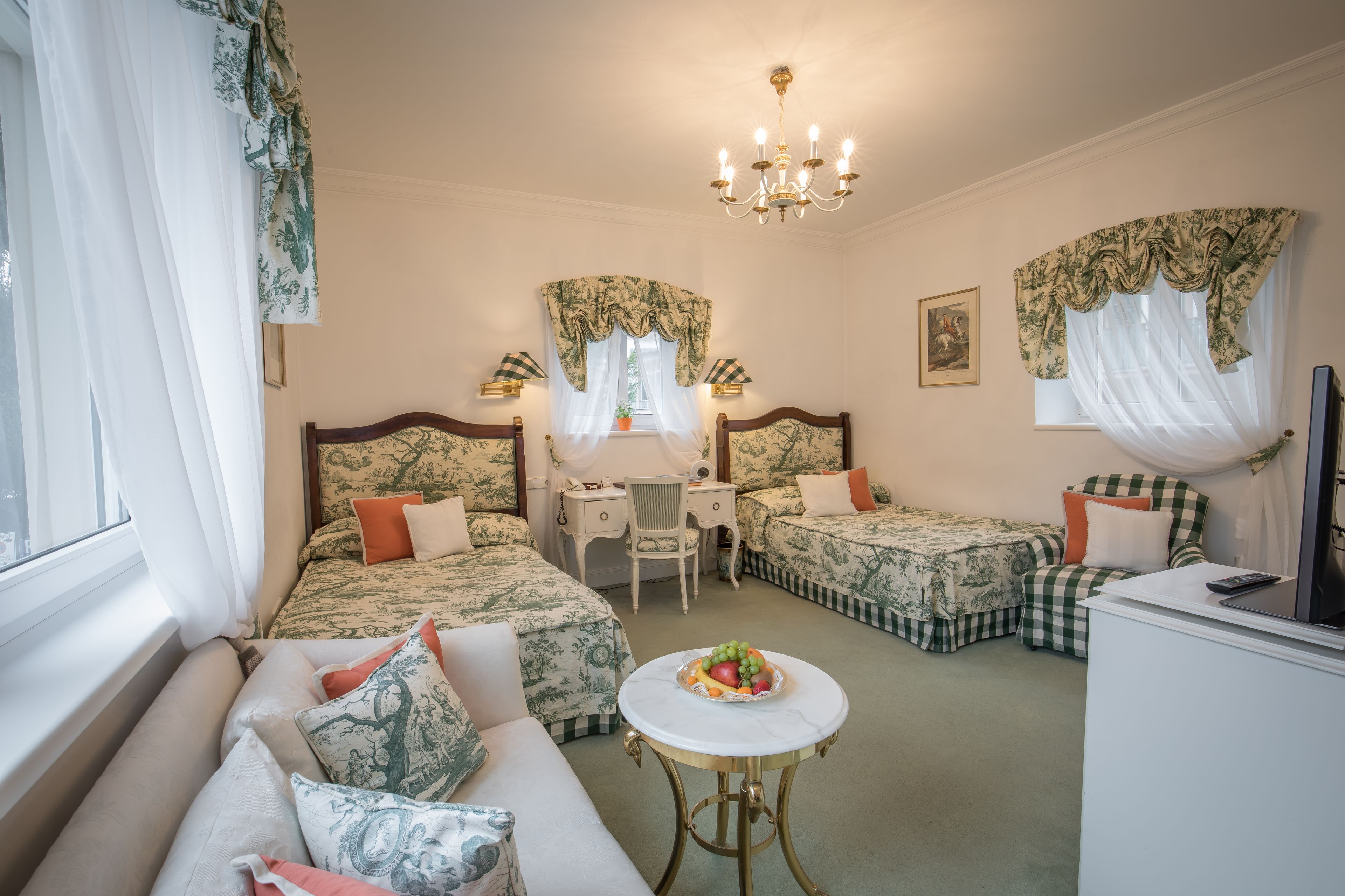 A hotel room with two beds, a sofa, a desk, a chair, a table with fruit, and a TV.