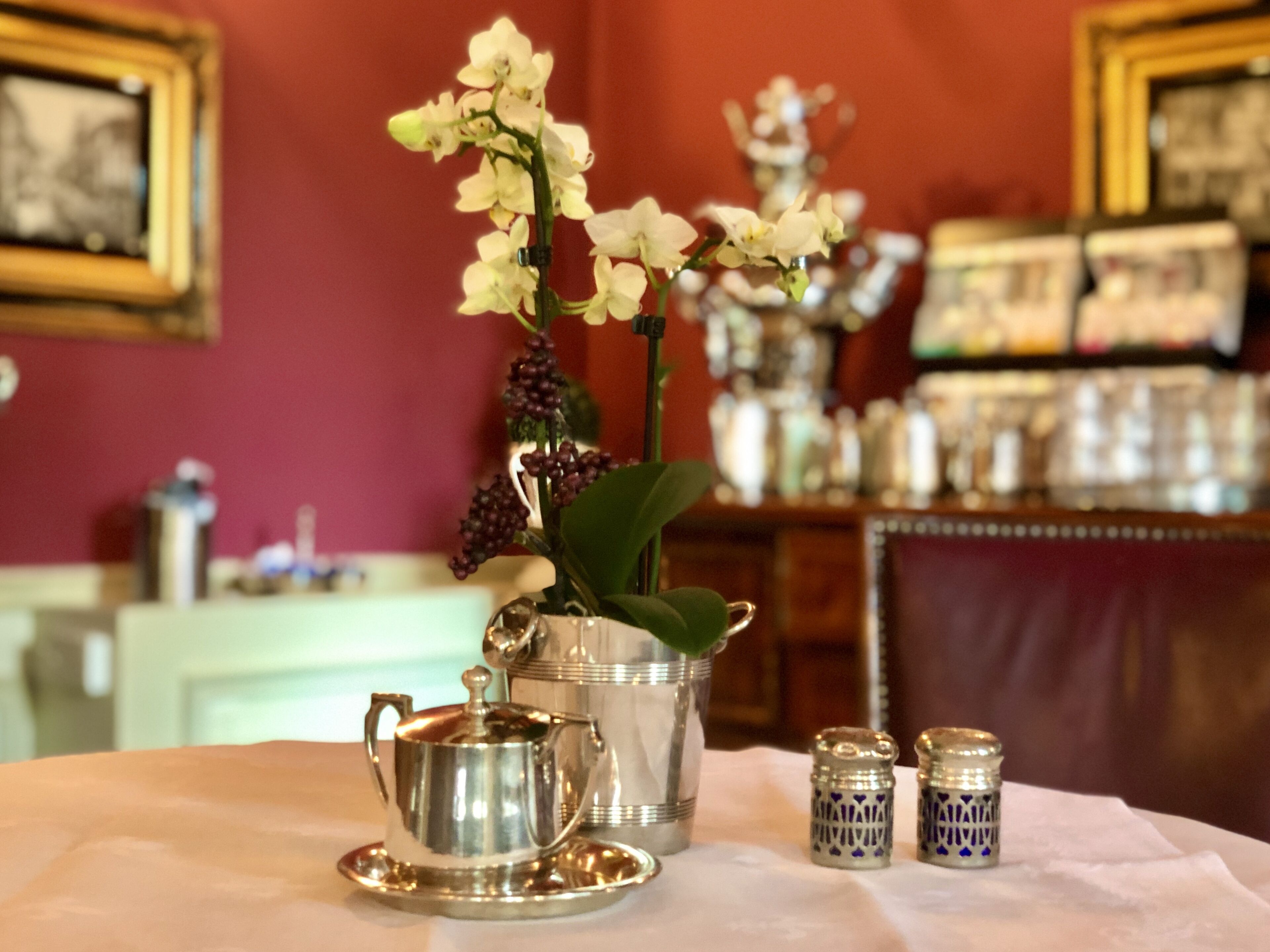 A table with a silver teapot, a silver sugar bowl, a silver creamer, and a silver creamer with a blue pattern. There is also a silver pitcher with a handle and a silver pitcher with a lid.