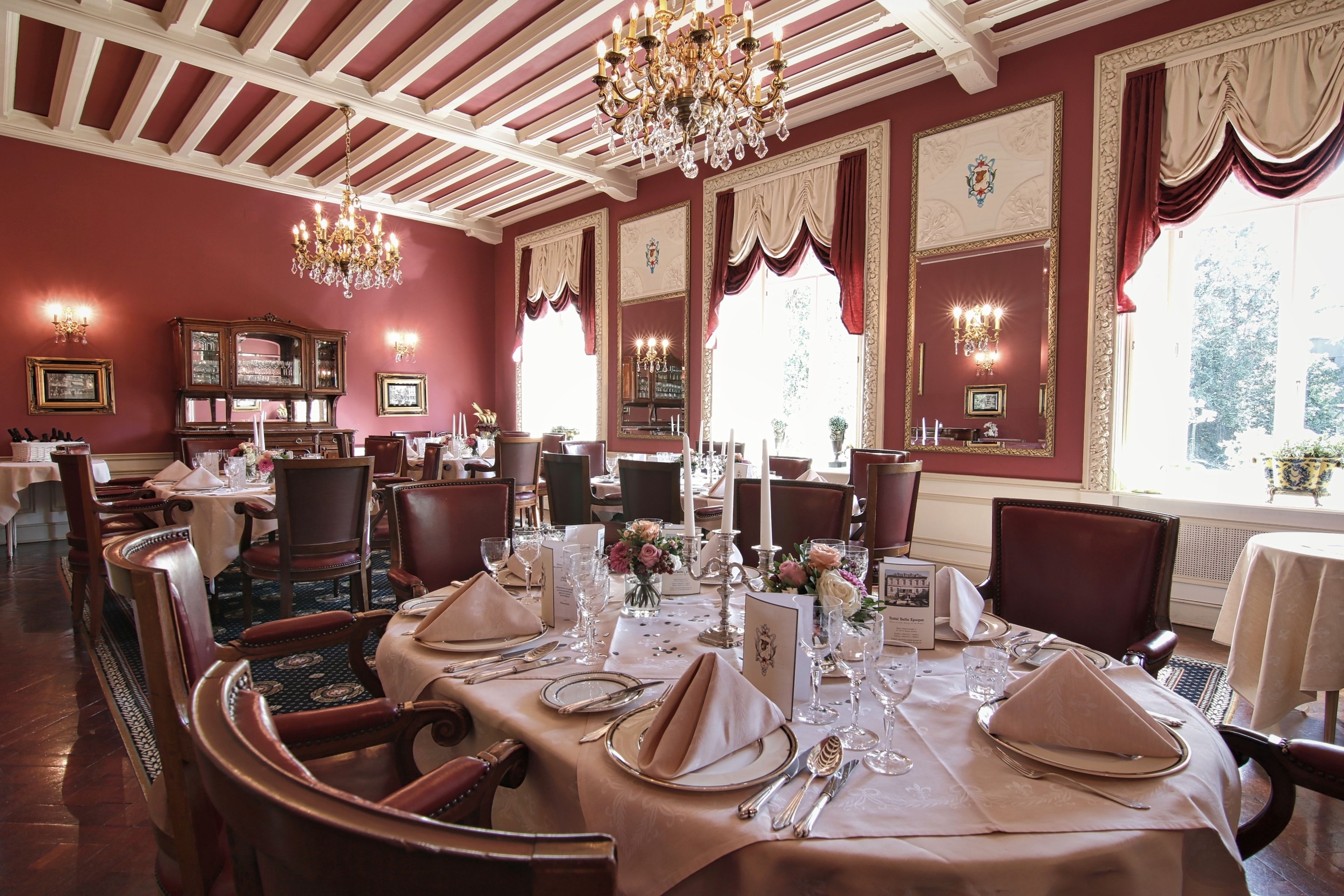 Uma sala de jantar formal com mesas postas, lustres e quadros nas paredes.