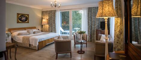 Ein Hotelzimmer mit einem großen Bett, zwei Sesseln, einem kleinen Tisch mit einer Vase, einer Lampe und einem Spiegel.