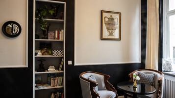 A room with a bookshelf, two chairs, a table, a framed picture, and a window with curtains.