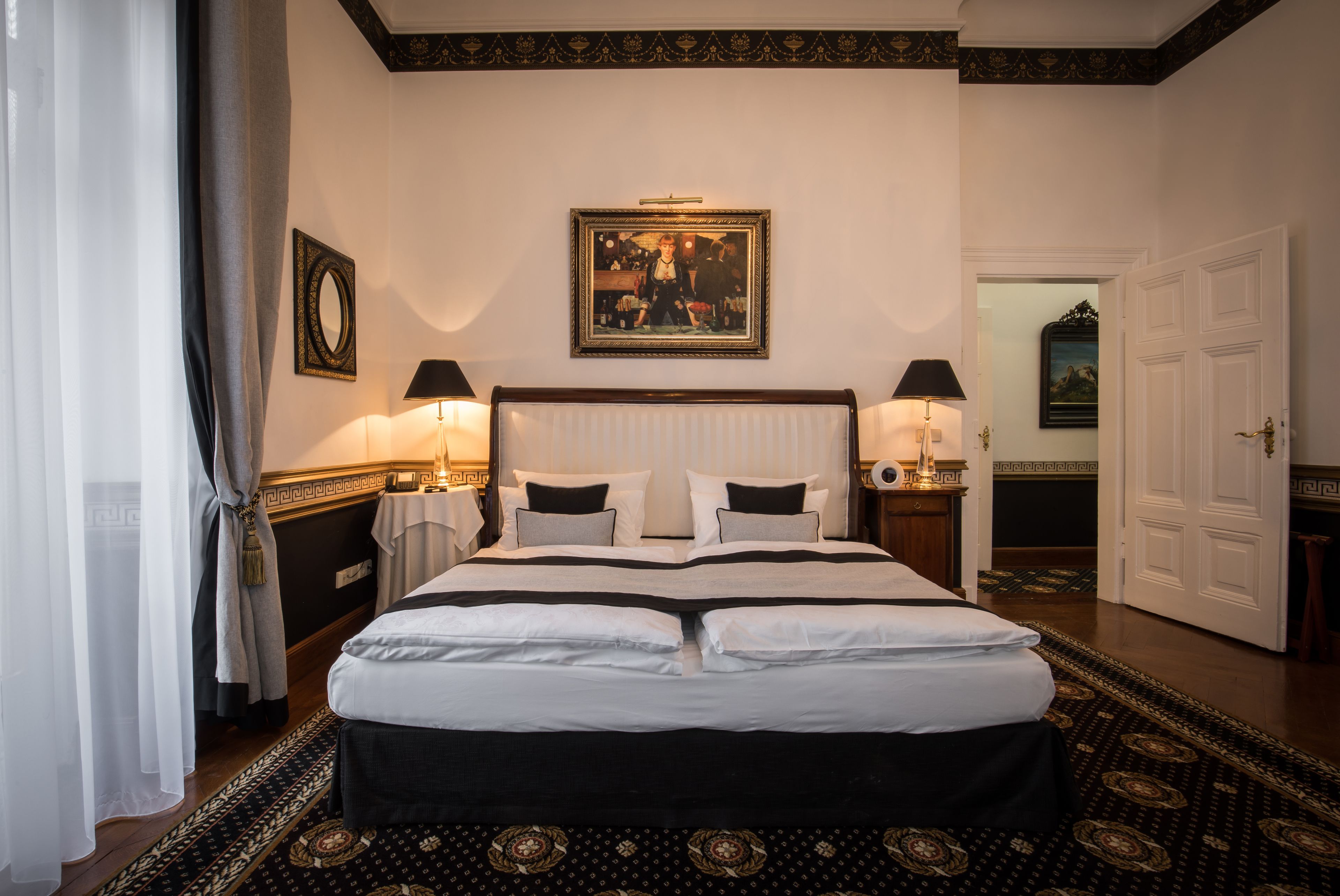 A neatly made bed with a white and black bedspread, two bedside lamps, a framed picture above the bed, and a patterned carpet.