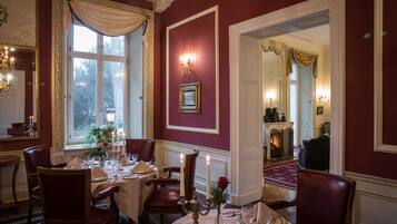 A formal dining room with a table set for four, a chandelier, and a fireplace in the background.