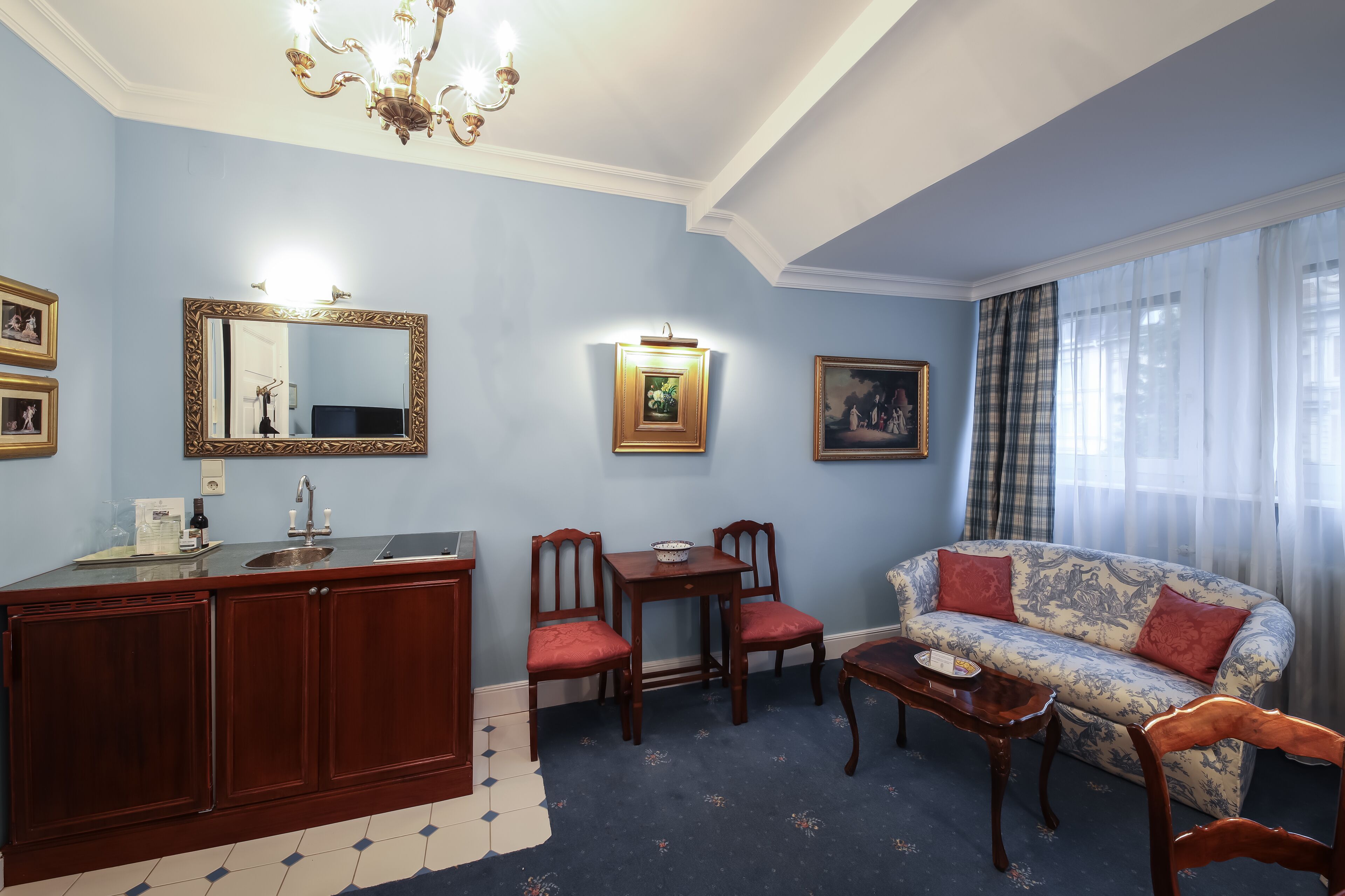 Ein Zimmer mit Esstisch, Stühlen, einer Couch, einer Kristallleuchtre und einem großen Spiegel.