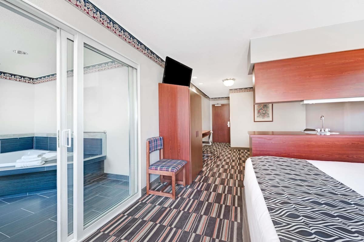 Une chambre d’hôtel dotée d’une douche en verre, d’une chaise en bois, d’un lit avec une couvre-lit à motifs et d’une coiffeuse en bois avec un lavabo.