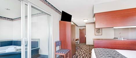 Une chambre d’hôtel dotée d’une douche en verre, d’une chaise en bois, d’un lit avec une couvre-lit à motifs et d’une coiffeuse en bois avec un lavabo.