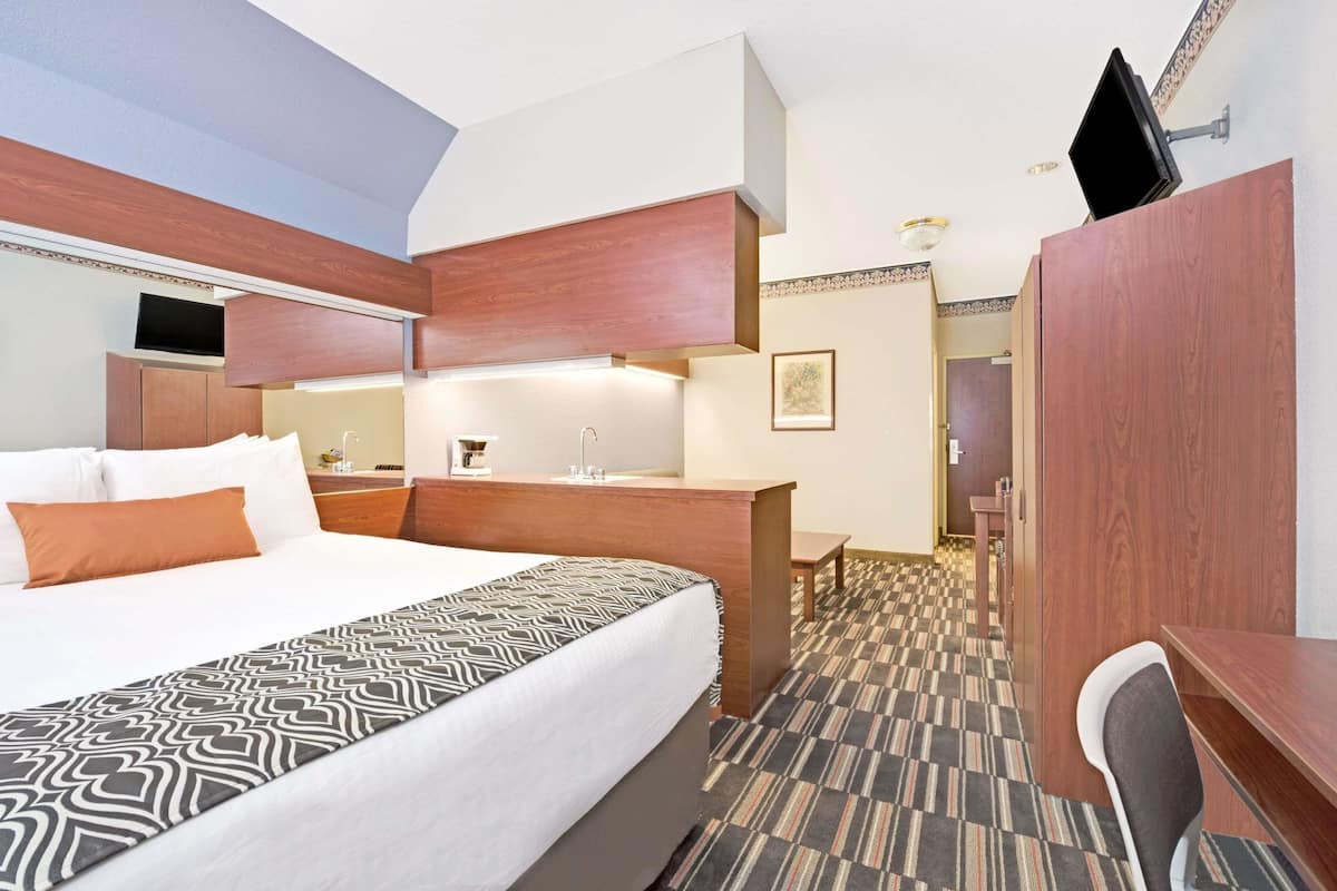 Une chambre d’hôtel avec un grand lit, un bureau, une chaise et un téléviseur fixé au mur.