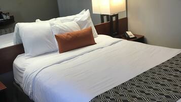 Habitación de hotel con una cama bien hecha, una lámpara de noche, un teléfono y una alfombra estampada.