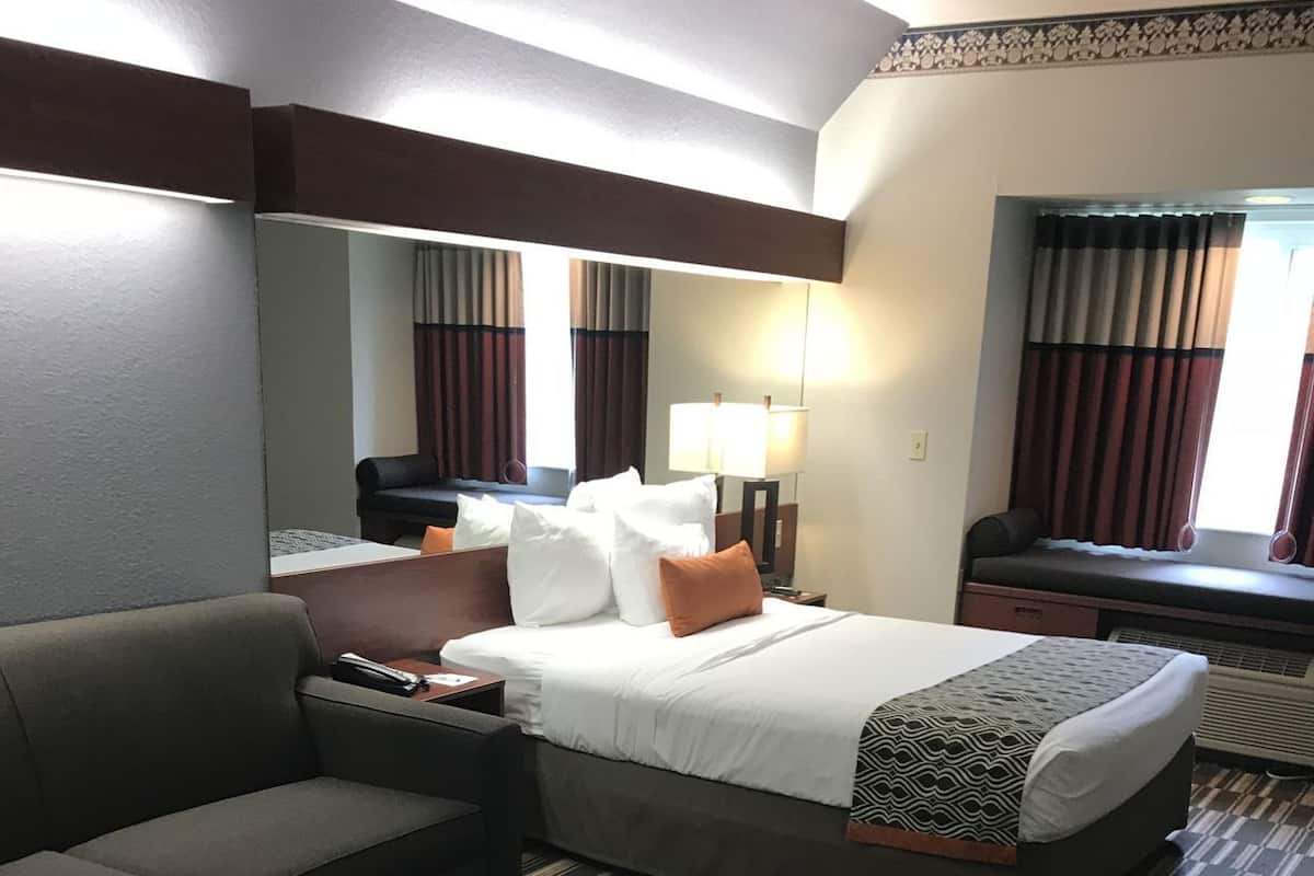 Une chambre d’hôtel avec un lit, un canapé, une petite table, une lampe et une fenêtre avec des rideaux.